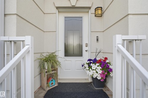 Entryway featuring a white paneled door with a decorative glass insert, a brass wall sconce, and white railing - #22 723 172 Street Sw, Edmonton, AB - Outdoor With Exterior