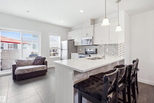 Bright kitchen featuring a white countertop island, stainless steel appliances, and light-toned cabinetry - #22 723 172 Street Sw, Edmonton, AB - Indoor Photo Showing Kitchen With Double Sink With Upgraded Kitchen