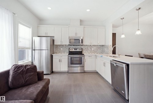 Modern kitchen featuring white cabinetry, stainless steel appliances, a mosaic tile backsplash, a kitchen island with sink, and recessed lighting - #22 723 172 Street Sw, Edmonton, AB - Indoor Photo Showing Kitchen With Upgraded Kitchen
