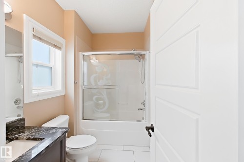 Bathroom featuring a white bathtub with a sliding glass enclosure, white toilet, and a vanity with a dark countertop and undermount sink - 5931 12 Avenue Sw, Edmonton, AB - Indoor Photo Showing Bathroom