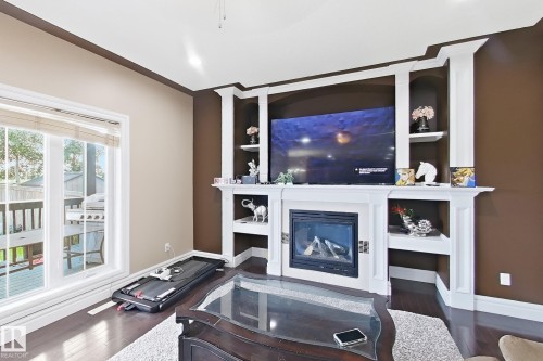 Living area with dark wood-finish flooring and a built-in entertainment center featuring a fireplace and integrated shelving - 5931 12 Avenue Sw, Edmonton, AB - Indoor Photo Showing Living Room With Fireplace