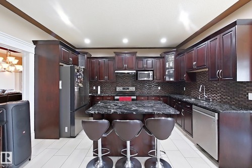 Gourmet kitchen featuring dark wood cabinetry, stainless steel appliances, a center island with bar seating, and a mosaic tile backsplash - 5931 12 Avenue Sw, Edmonton, AB - Indoor Photo Showing Kitchen With Upgraded Kitchen