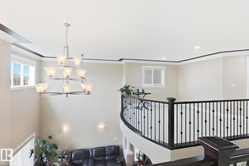 Open upper-level landing featuring a wrought iron railing, dark wood-finish handrail, and an elegant multi-tiered chandelier - 5931 12 Avenue Sw, Edmonton, AB - Indoor Photo Showing Other Room