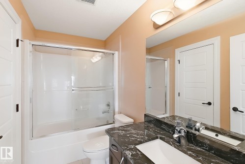 Bathroom featuring a shower-over-tub combination with sliding glass doors, a vanity with a dark stone-finish countertop, an undermount sink, and a large wall mirror - 5931 12 Avenue Sw, Edmonton, AB - Indoor Photo Showing Bathroom