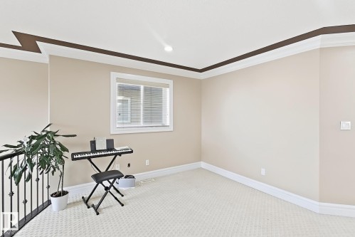 Carpeted room featuring a window with blinds, crown molding, and a black wrought iron railing - 5931 12 Avenue Sw, Edmonton, AB - Indoor