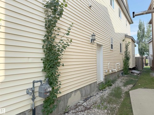 Cream-colored vinyl siding exterior with a side entry door, an exterior wall light fixture, and a concrete pathway - 5931 12 Avenue Sw, Edmonton, AB - Outdoor With Exterior