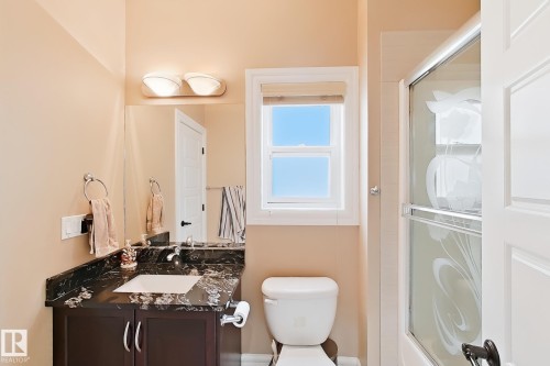 Contemporary bathroom featuring a dark wood vanity with a stone countertop, an integrated rectangular sink, a frameless mirror, and a white framed window - 5931 12 Avenue Sw, Edmonton, AB - Indoor Photo Showing Bathroom