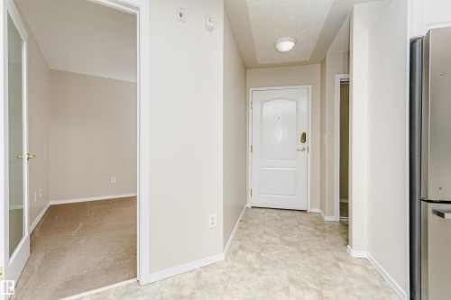 Entryway featuring a white paneled door with brass hardware, light-toned flooring, and a flush mount ceiling light - #413 237 Youville Dr E Nw, Edmonton, AB - Indoor Photo Showing Other Room
