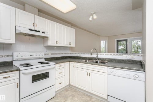 Kitchen featuring white cabinetry, gray countertops, a stainless steel double basin sink, and white appliances including a range and dishwasher - #413 237 Youville Dr E Nw, Edmonton, AB - Indoor Photo Showing Kitchen With Double Sink