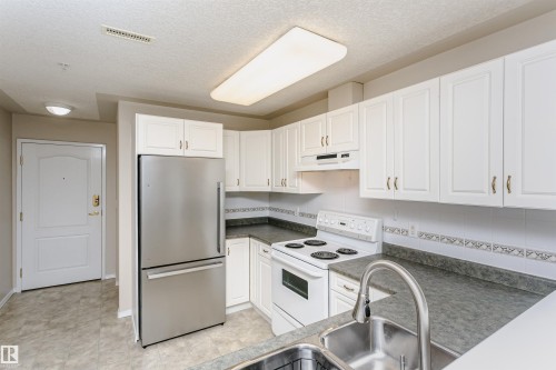 Kitchen featuring white cabinetry, a stainless steel refrigerator, white range, double basin sink, and laminate countertops - #413 237 Youville Dr E Nw, Edmonton, AB - Indoor Photo Showing Kitchen
