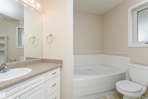 Bathroom featuring a corner soaking tub, white vanity with integrated sink, large wall mirror, and a window with privacy glass - #413 237 Youville Dr E Nw, Edmonton, AB - Indoor Photo Showing Bathroom