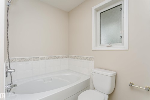 Full bathroom featuring an integrated shower/tub combination with chrome fixtures, a tiled surround with decorative trim, and a window with frosted glass - #413 237 Youville Dr E Nw, Edmonton, AB - Indoor Photo Showing Bathroom
