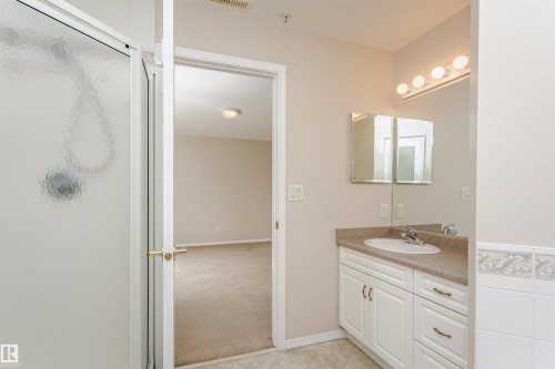 Bathroom featuring a white vanity with integrated sink, coordinating countertop, and a large mirror with a four-bulb vanity light fixture - #413 237 Youville Dr E Nw, Edmonton, AB - Indoor Photo Showing Bathroom
