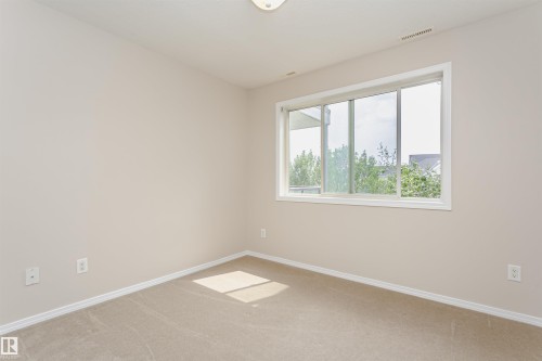 Neutral-toned carpeting and walls, featuring a wide window with white trim, and a flush-mount ceiling light fixture - #413 237 Youville Dr E Nw, Edmonton, AB - Indoor Photo Showing Other Room