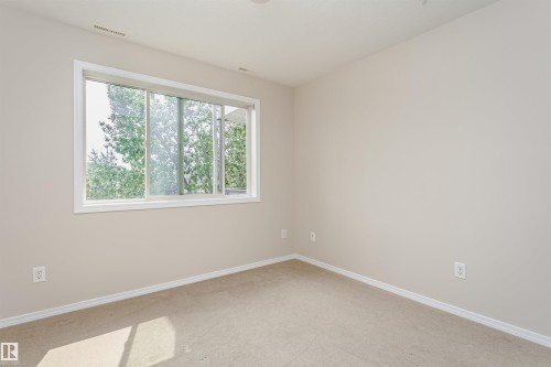 Neutral tone walls, carpet flooring, and a large window featuring outdoor foliage - #413 237 Youville Dr E Nw, Edmonton, AB - Indoor Photo Showing Other Room