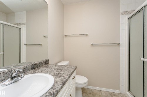 Bathroom featuring a white vanity with a speckled countertop, an integrated sink, a chrome faucet, and a large wall-mounted mirror - #413 237 Youville Dr E Nw, Edmonton, AB - Indoor Photo Showing Bathroom