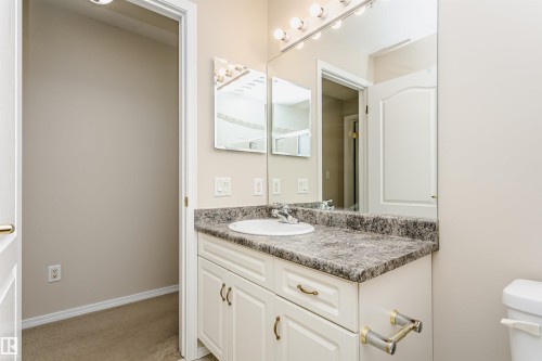 Vanity featuring a built-in sink, speckled countertop, and white cabinetry with brass-finish hardware - #413 237 Youville Dr E Nw, Edmonton, AB - Indoor Photo Showing Bathroom