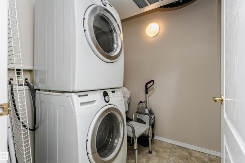 Dedicated laundry area featuring stacked front-load machines, neutral wall paint, and tiled flooring - #413 237 Youville Dr E Nw, Edmonton, AB - Indoor Photo Showing Laundry Room