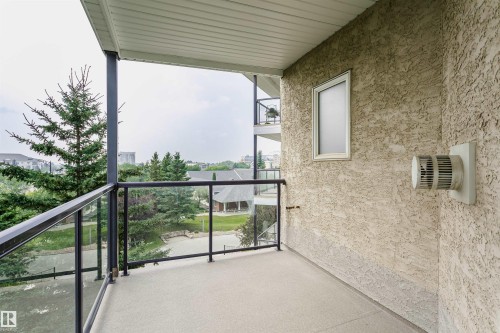 Outdoor balcony featuring a concrete floor, glass railing with black framing, and a textured stucco exterior wall - #413 237 Youville Dr E Nw, Edmonton, AB - Outdoor With Balcony With Exterior
