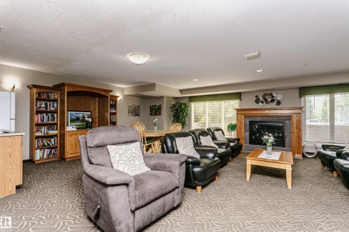 Spacious common room featuring a built-in fireplace with a stone surround and wood mantel - #413 237 Youville Dr E Nw, Edmonton, AB - Indoor Photo Showing Living Room With Fireplace