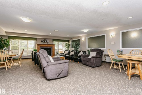 Spacious common area featuring patterned carpeting, recessed lighting, and large windows with blinds - #413 237 Youville Dr E Nw, Edmonton, AB - Indoor Photo Showing Other Room With Fireplace
