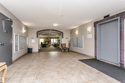 Entryway featuring tile flooring, wall-mounted mailboxes, an elevator with decorative framing, a gray access door, and an arched entryway to a common area with a fireplace - #413 237 Youville Dr E Nw, Edmonton, AB - Indoor Photo Showing Other Room