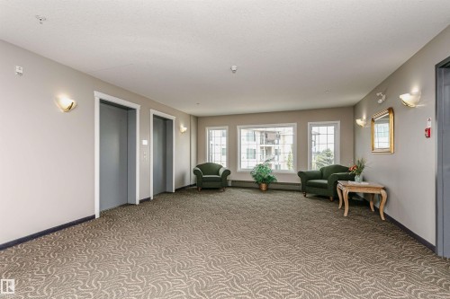 Building common area featuring patterned carpet flooring, two elevators, multiple wall sconces, and a window bank offering exterior views - #413 237 Youville Dr E Nw, Edmonton, AB - Indoor Photo Showing Other Room