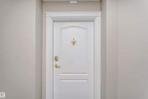 White paneled entry door with decorative brass door knocker and hardware - #413 237 Youville Dr E Nw, Edmonton, AB -  With Exterior