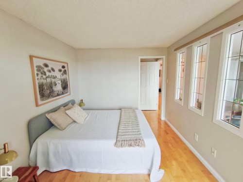 Light-filled interior featuring wood-finish flooring, multiple windows with white trim, a solid panel interior door, and neutral wall paint - #509 10149 Saskatchewan Dr Nw, Edmonton, AB - Indoor Photo Showing Bedroom