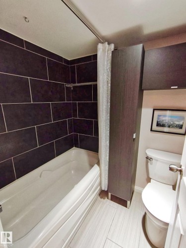 Bathroom featuring a shower/tub combination with dark rectangular wall tiling, white tub, light-toned plank flooring, and a white toilet - #509 10149 Saskatchewan Dr Nw, Edmonton, AB - Indoor Photo Showing Bathroom