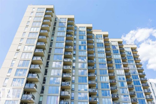 Contemporary high-rise building featuring a light-toned facade, numerous balconies with glass railings, large windows, and a stepped architectural design - #509 10149 Saskatchewan Dr Nw, Edmonton, AB - Outdoor With Facade