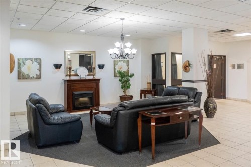 Lounge area featuring a fireplace with a wood mantel, decorative mirror, and a chandelier - #509 10149 Saskatchewan Dr Nw, Edmonton, AB - Indoor With Fireplace