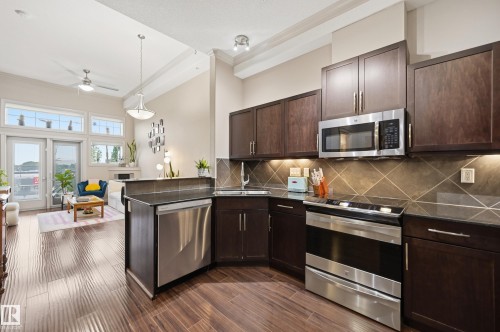 Kitchen featuring dark wood-finish cabinetry, stainless steel appliances, and a tiled backsplash - #443 10121 80 Av Nw, Edmonton, AB - Indoor Photo Showing Kitchen With Upgraded Kitchen