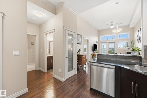 Open concept living space featuring wood-finish flooring, high ceilings, recessed lighting, and a kitchen with dark cabinetry, stainless steel dishwasher, and dark countertops - #443 10121 80 Av Nw, Edmonton, AB - Indoor Photo Showing Kitchen
