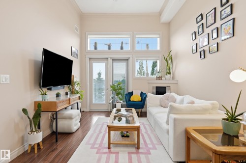 Living area featuring wood-finish flooring, a white fireplace with a mantel, and French doors with transom windows - #443 10121 80 Av Nw, Edmonton, AB - Indoor Photo Showing Living Room