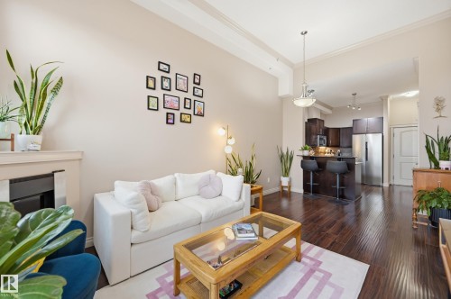 Open-concept living space featuring wood-finish flooring, a contemporary fireplace with a light-colored mantel, and high ceilings with crown molding - #443 10121 80 Av Nw, Edmonton, AB - Indoor Photo Showing Living Room With Fireplace