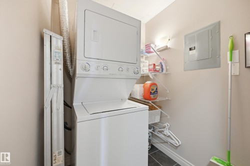Dedicated laundry area featuring a stackable washer and dryer, tile flooring, and integrated shelving - #443 10121 80 Av Nw, Edmonton, AB - Indoor Photo Showing Laundry Room