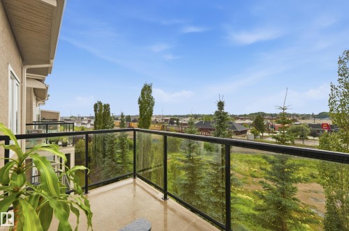 Balcony featuring a glass railing with black metal supports, stucco exterior, and surrounding natural foliage - #443 10121 80 Av Nw, Edmonton, AB - Outdoor With Balcony With View