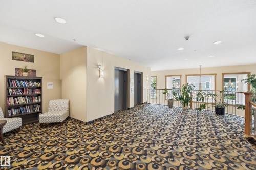 Spacious common area featuring patterned carpeting, recessed lighting, two elevators, and a built-in bookshelf - #443 10121 80 Av Nw, Edmonton, AB - Indoor