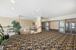Spacious interior corridor with patterned carpet flooring, recessed ceiling lighting, a wood and metal railing system, and multiple glass-paneled doors - 