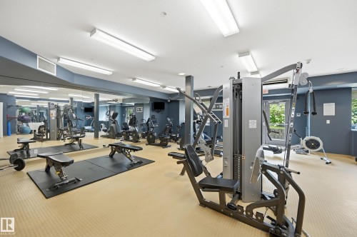 Dedicated fitness room featuring multiple exercise machines, full-height mirrored wall, recessed lighting, and patterned flooring - #443 10121 80 Av Nw, Edmonton, AB - Indoor Photo Showing Gym Room