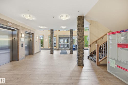 Building lobby featuring two stainless steel elevators, stacked stone columns, and wood-finish flooring - #443 10121 80 Av Nw, Edmonton, AB - Indoor Photo Showing Other Room