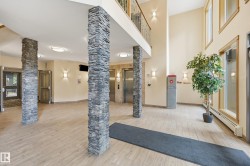 Spacious lobby featuring stacked stone columns, light wood-finish flooring, and a second-story balcony with metal railings - 