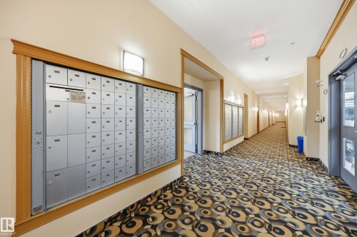 Building corridor featuring a patterned carpet, recessed wall sconces, and a large bank of individual mailboxes framed with wood trim - #443 10121 80 Av Nw, Edmonton, AB - Indoor Photo Showing Other Room