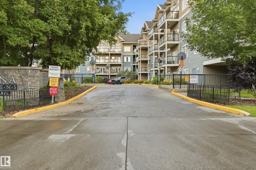 Gated entrance with smooth asphalt driveway featuring yellow-painted curbs and black iron fencing - #443 10121 80 Av Nw, Edmonton, AB - Outdoor With Balcony With Facade