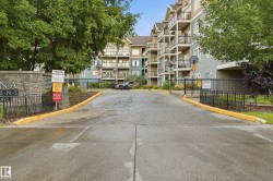 Gated entrance with smooth asphalt driveway featuring yellow-painted curbs and black iron fencing - 