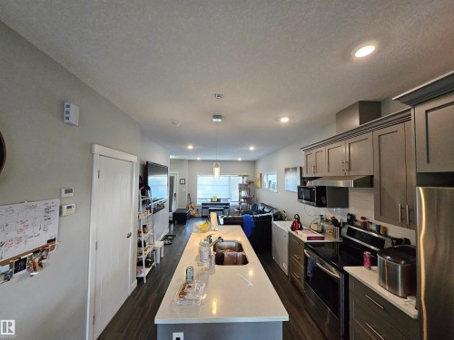 Open concept kitchen featuring an extended island with a double sink, gray cabinetry, stainless steel appliances, and wood-finish flooring - 13309 104 Street Nw, Edmonton, AB - Indoor Photo Showing Kitchen With Upgraded Kitchen