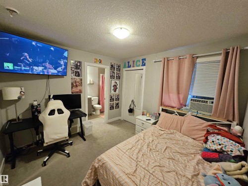 Carpeted room featuring a ceiling-mounted light fixture, an integrated wall air conditioning unit, and a doorway leading to an additional space - 13309 104 Street Nw, Edmonton, AB - Indoor Photo Showing Bedroom
