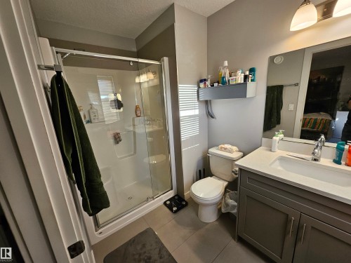 Bathroom featuring a glass-enclosed shower with a white surround, a single-basin vanity with a light-colored countertop, gray cabinet storage, and a wall-mounted mirror with integrated lighting - 13309 104 Street Nw, Edmonton, AB - Indoor Photo Showing Bathroom
