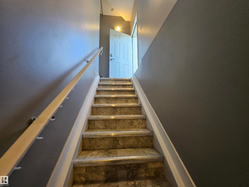 Staircase featuring tiled treads, white risers, a light wood-finish handrail, and a two-tone wall with a gray upper section - 13309 104 Street Nw, Edmonton, AB - Indoor Photo Showing Other Room